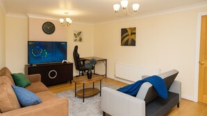 Een woonkamer met een bank, een salontafel, een televisie, een game stoel en een radiator.