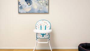 Een baby hoogstoel met stippen patroon en een witte lade, in een kamer met houten vloer en een effen muur.