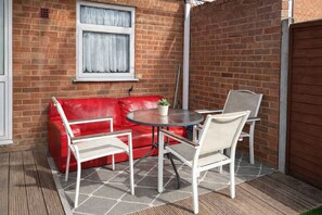 Un sofá de cuero rojo, una mesa redonda y cuatro sillas en un patio con pared de ladrillo y ventana.