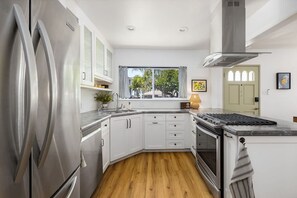 A modern kitchen with white cabinets, a stainless steel refrigerator, a built-in oven, and a window with a view of the outdoors. - Carlsbad Cottage - Remodeled (Carlsbad)