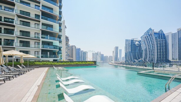 A modern hotel with a swimming pool, lounge chairs, and a view of the city skyline.
