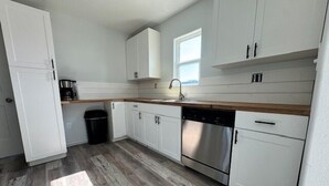 Una cocina moderna con armarios blancos, lavavajillas de acero inoxidable y encimera de madera.
