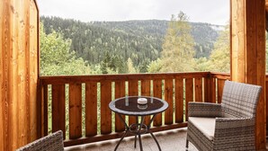 A wooden balcony with a round table and two wicker chairs, overlooking a forested hillside. - Apartment in Kreischberg Near Ski Resort (Sankt Georgen am Kreischberg)