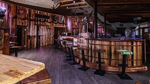 A rustic bar area with wooden walls and furniture, a counter with stools, and a wooden table. - Apartment in Kreischberg Near Ski Resort (Sankt Georgen am Kreischberg)