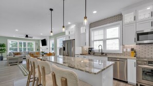 A modern kitchen with white cabinets, a large island, stainless steel appliances, and pendant lighting.