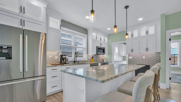 A modern kitchen with white cabinetry, stainless steel appliances, and a central island with bar stools.