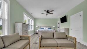 A bedroom with a bed, a sofa, a nightstand, a dresser, and a ceiling fan.