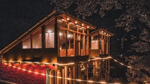 A wooden cabin with large windows, a red roof, and string lights. - WOW Treehouse & Cottages (Jibhi)