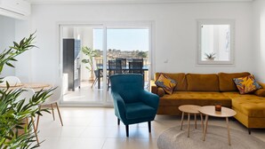 A modern living room with a blue armchair, a mustard sofa, and a dining area with white chairs and a table. - Stunning 2-baths apartment with golf and lake view (Sucina)