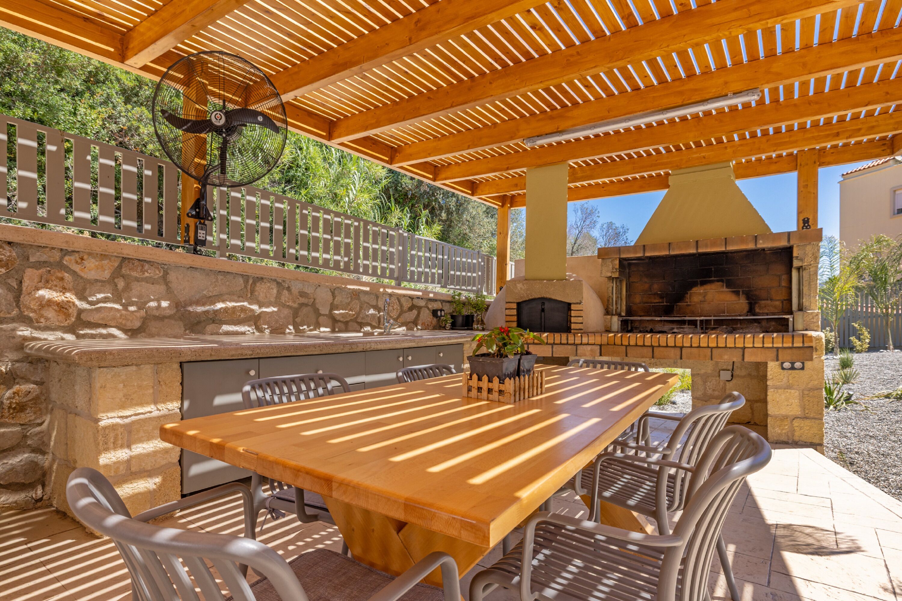Een terras buiten met een stenen openhaard, een houten tafel en metalen stoelen.