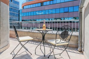 A balcony with a round table, two chairs, a bottle of champagne, and a view of modern buildings. - Rooftop Terrace Apartment (Zagreb)