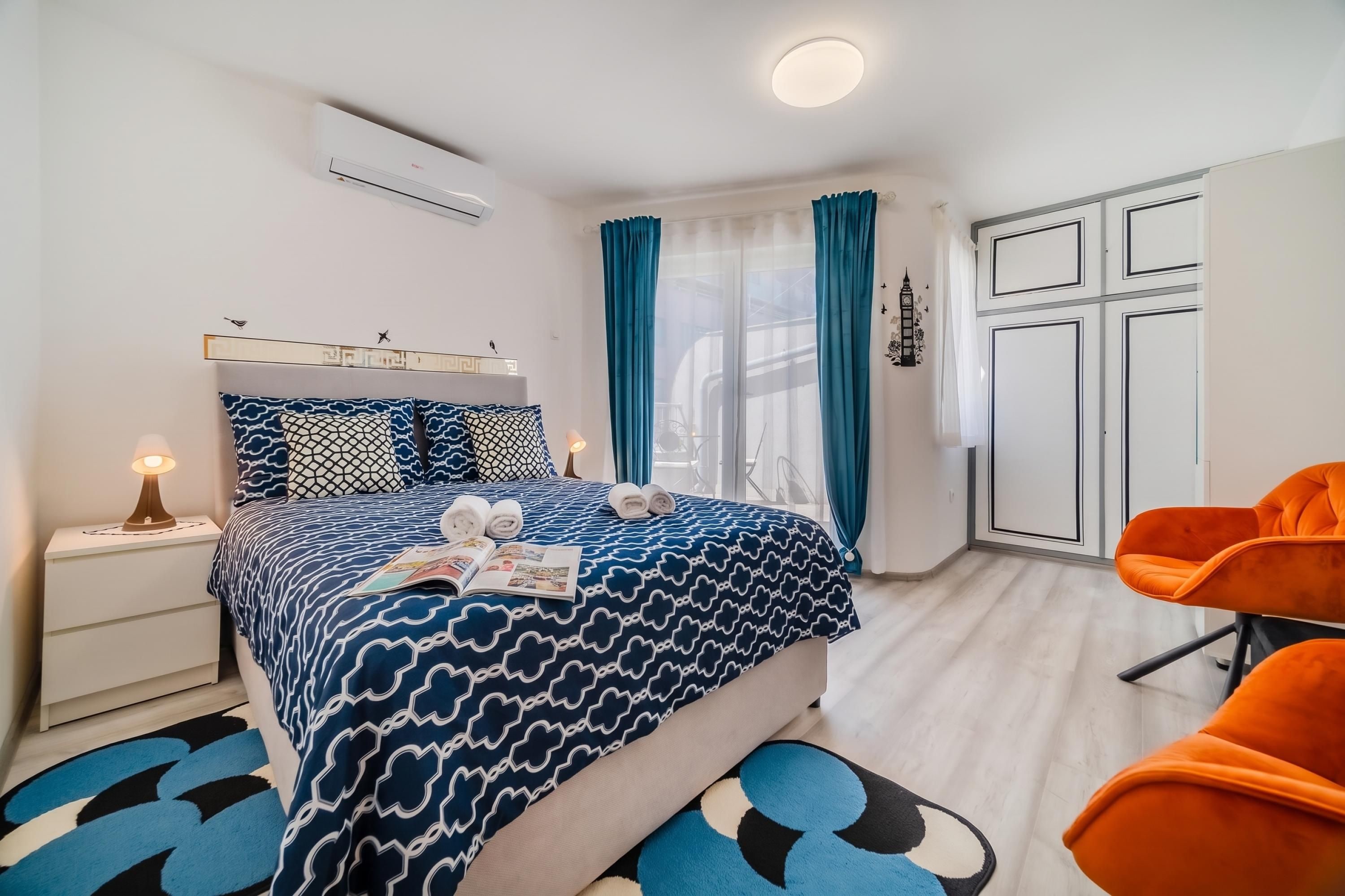 A modern bedroom with a bed, a nightstand, a reading lamp, a chair, and a wardrobe.