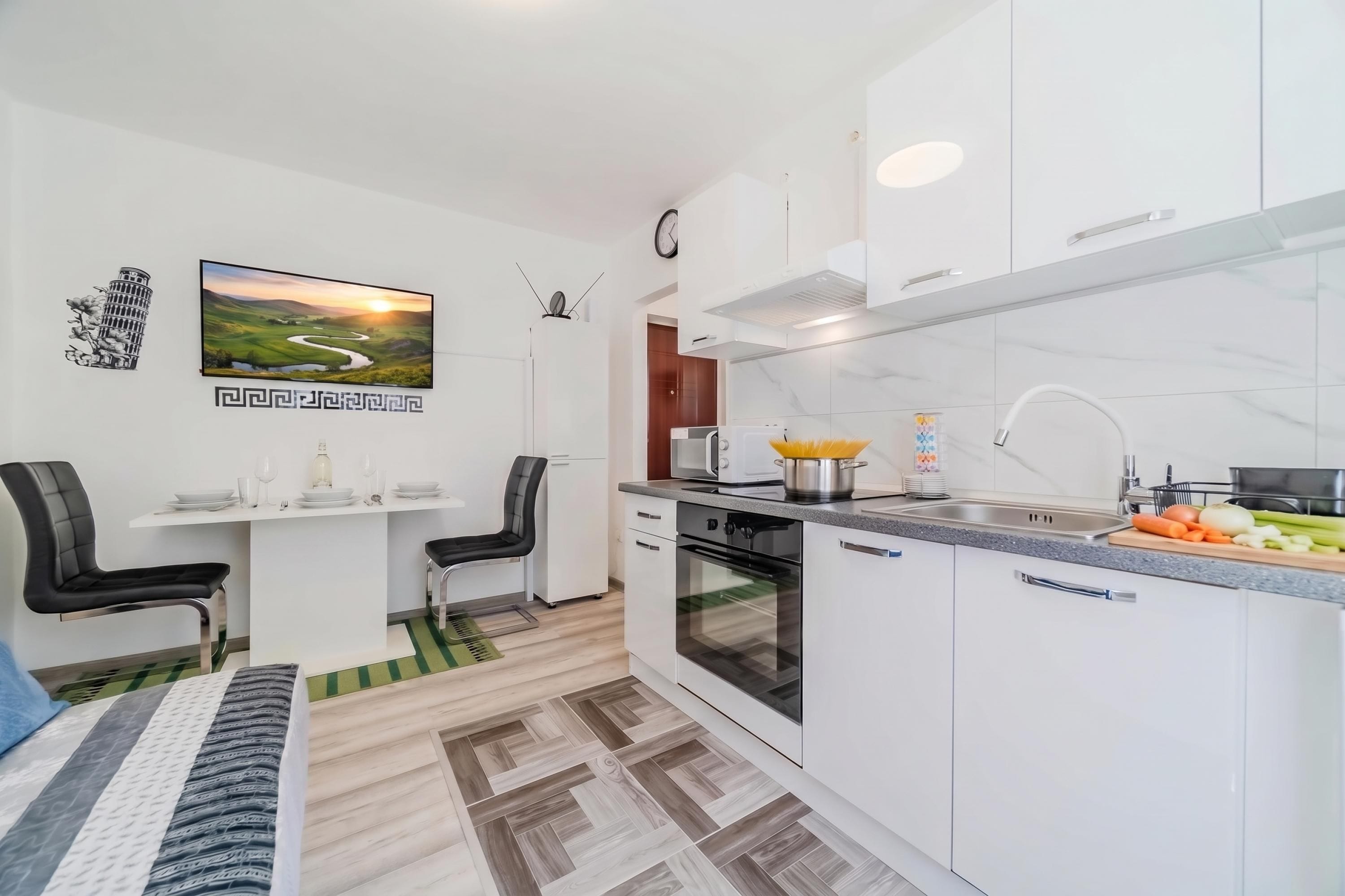 A modern kitchen with white cabinets, a built-in oven, a sink, and a dining area with a table and chairs.
