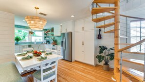A modern kitchen with white cabinetry, a stainless steel refrigerator, and a wooden spiral staircase. - Walk to Gulf: Luxe Luau-themed Gem in Holmes Beach (Holmes Beach)
