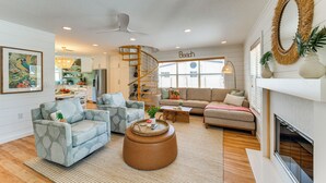 A spacious living room with a spiral staircase, a fireplace, and a kitchen in the background. - Walk to Gulf: Luxe Luau-themed Gem in Holmes Beach (Holmes Beach)