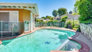 Uma piscina com design curvo, rodeada por um deck de tijolos e uma cerca branca.