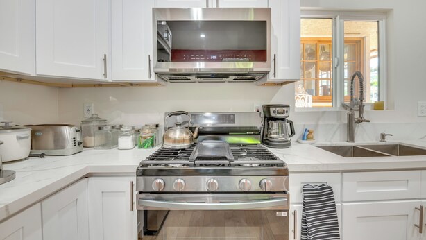 Uma cozinha moderna com armários brancos, um fogão de aço inoxidável, micro-ondas e pia.