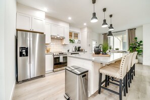 A modern kitchen with stainless steel appliances, white cabinetry, and a central island with bar stools. - 4 Mi to Dtwn: Modern Tacoma Home w/ Spacious Yard (Tacoma)