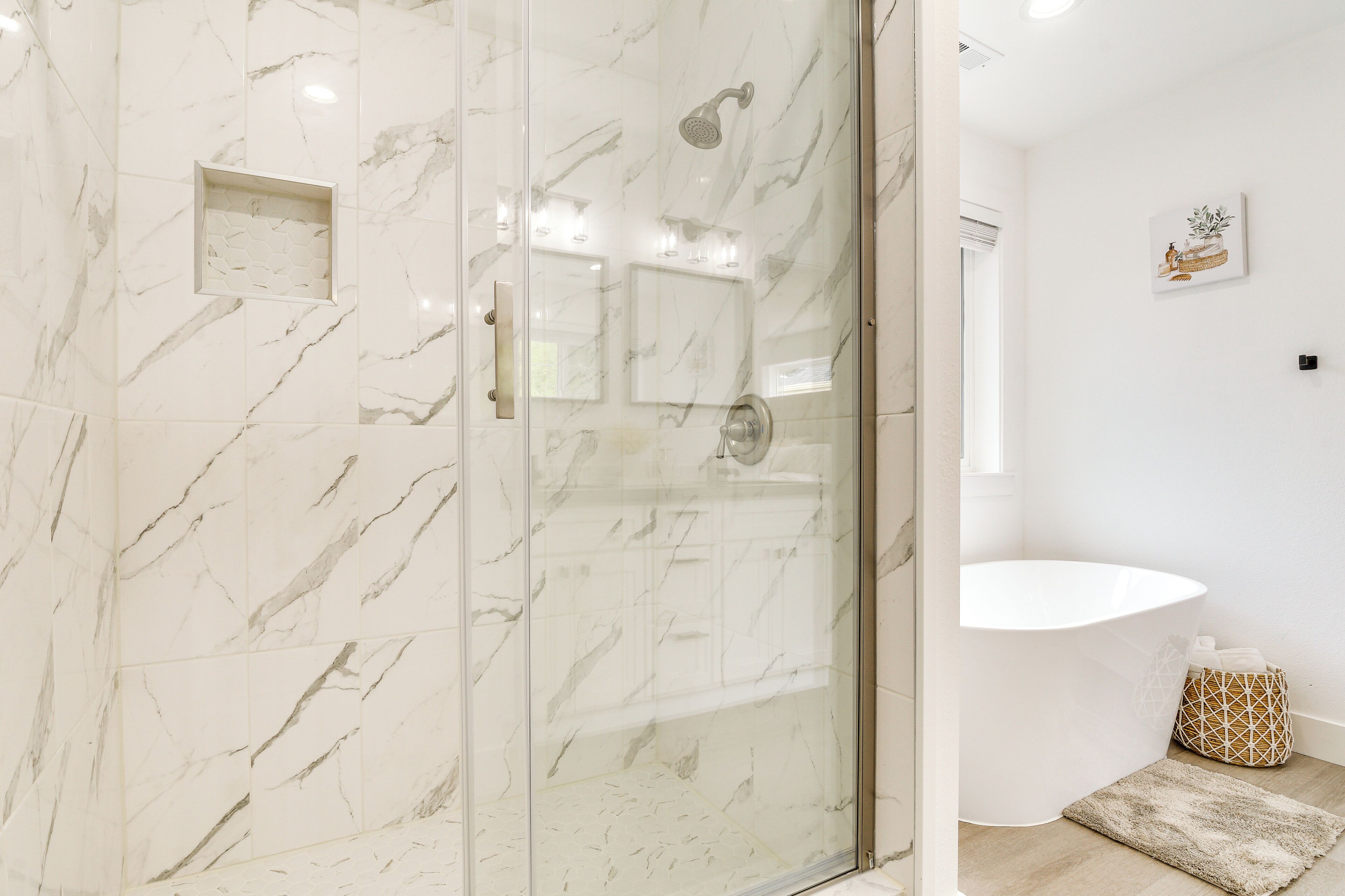 Un baño moderno con ducha de vidrio, suelo de mármol, lavamanos blanco y un pequeño estante decorativo.