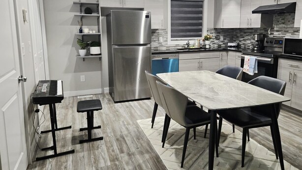 A modern kitchen with white cabinets, a stainless steel refrigerator, a built-in oven, and a dining area with a marble table and chairs.