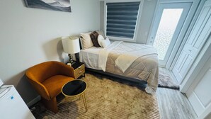 Ein Schlafzimmer mit einem Bett, einem Sessel, einem Nachttisch, einer Lampe und einem Fenster.