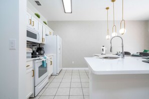 Une cuisine moderne avec des meubles blancs, un îlot central, un four encastré et un évier en acier inoxydable.