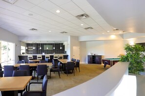 A modern indoor space with multiple tables and chairs, a pool table, and a plant.