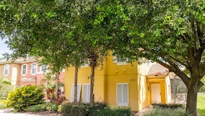 Un bâtiment jaune portant le numéro 8523, entouré de verdure et bordé d’un trottoir.