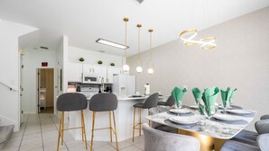 A modern kitchen with white cabinets, a central island, and a dining area with a marble table and grey chairs. - Gorgeous 4Bd w Pool at Encantada Resort 8523 (Kissimmee)