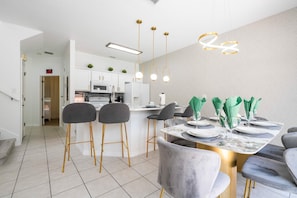 A modern kitchen with white cabinets, a central island, and a dining area with a marble table and grey chairs. - Gorgeous 4Bd w Pool at Encantada Resort 8523 (Kissimmee)