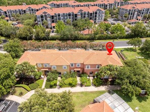 A multi-story residential building with a red-tiled roof, surrounded by lush greenery and a parking area. - Gorgeous 4Bd w Pool at Encantada Resort 8523 (Kissimmee)