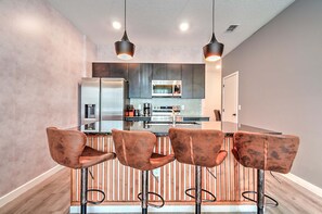 A modern kitchen with a central island, bar stools, pendant lighting, and stainless steel appliances. - 3417 Brand New 3BD Family Home Near Disney (Kissimmee)