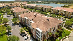 A residential complex with multiple apartment buildings, a parking area, and a lake in the background.