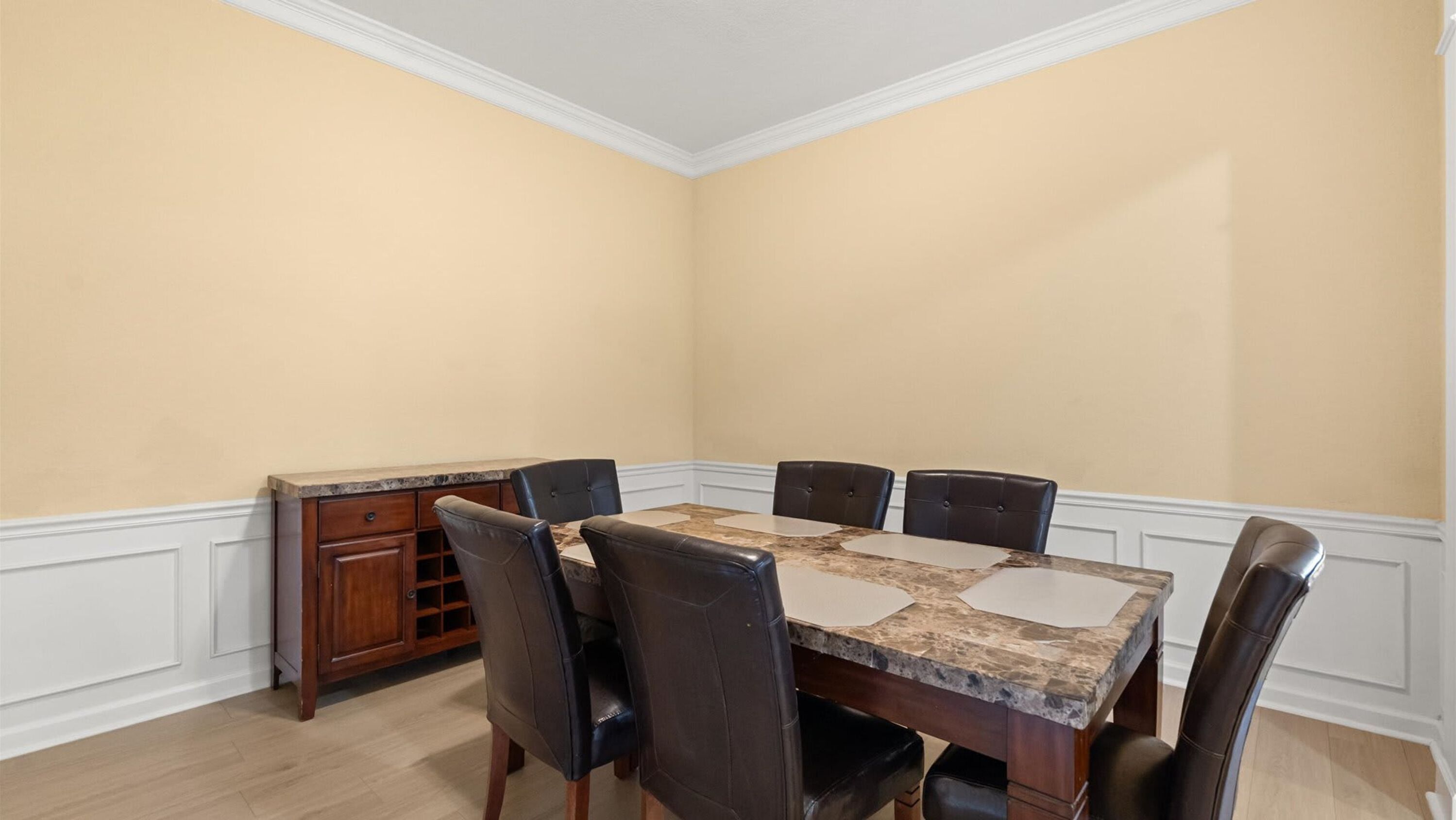 Une salle à manger avec une table en marbre, six chaises et un buffet en bois.