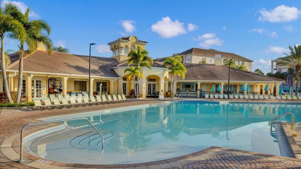 A swimming pool with lounge chairs and a building with a tiled roof and arched windows.