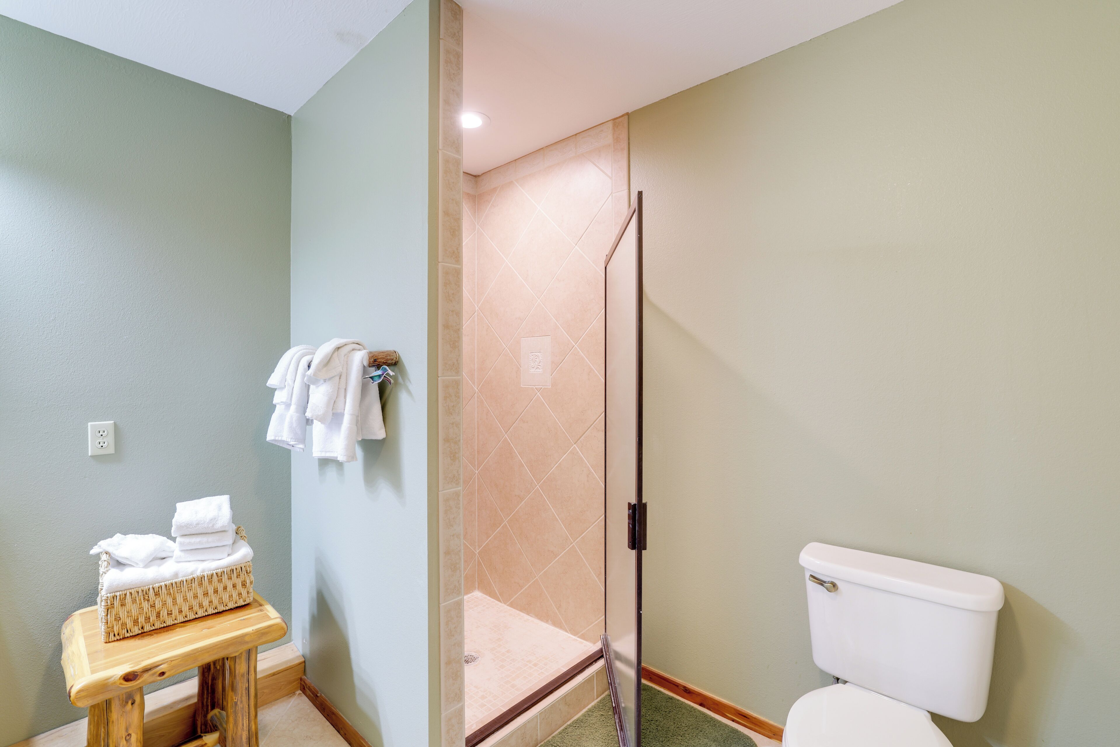 A bathroom with a shower, toilet, and a small table with towels.