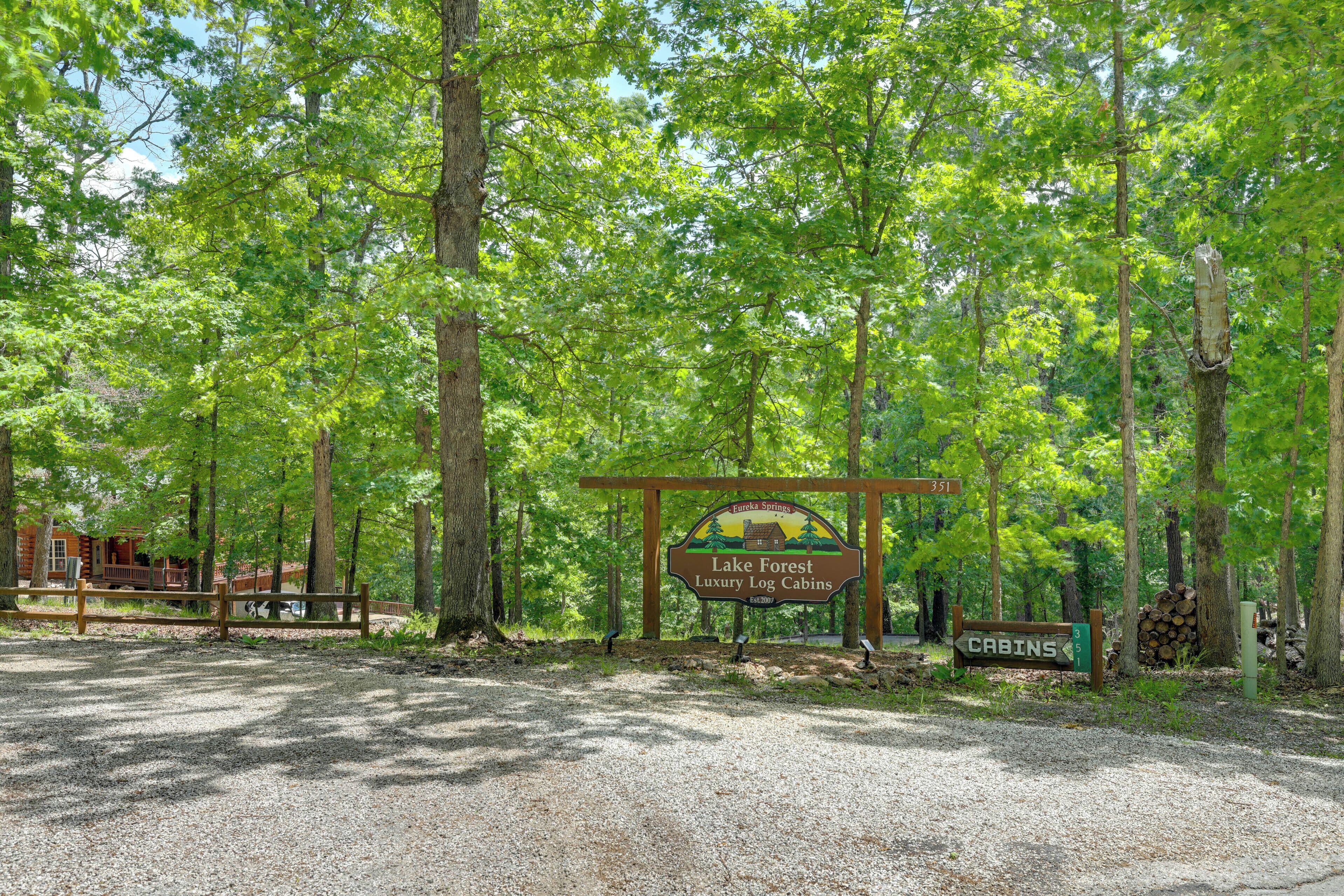 A sign for Lake Forest Luxury Log Cabins with a gravel path leading to the cabins.