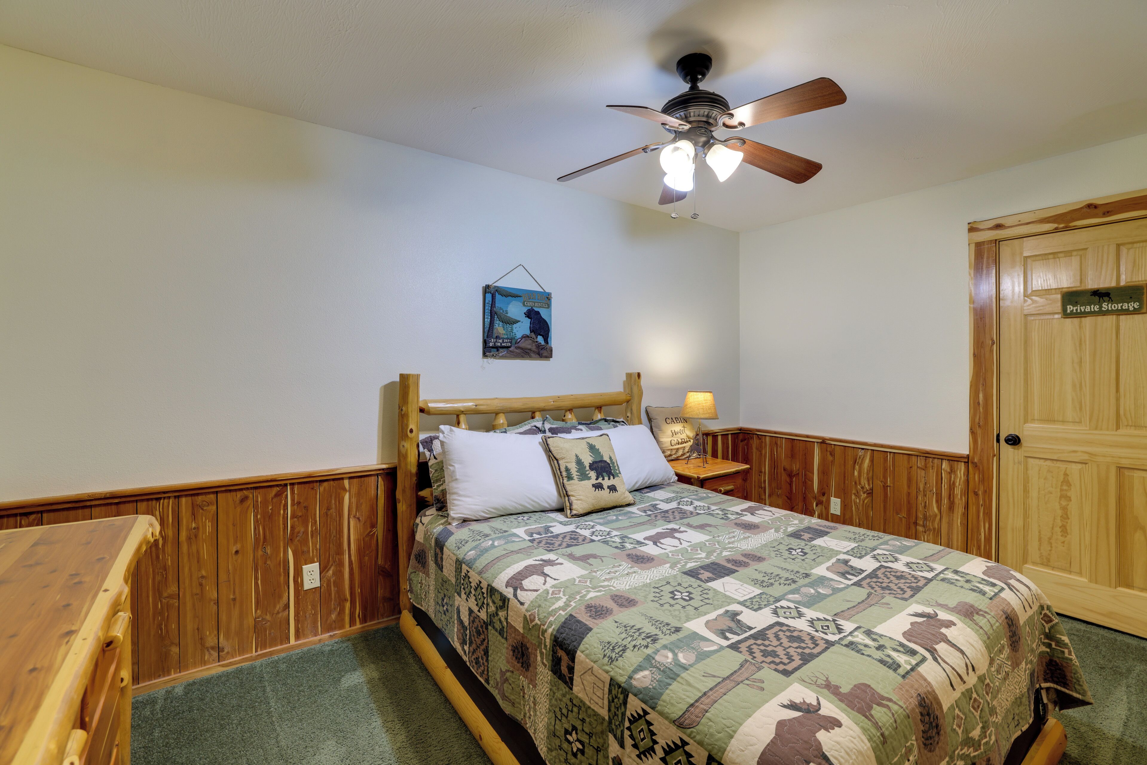A bedroom with a wooden headboard, a quilted bedspread, a ceiling fan, a nightstand with a lamp, and a door labeled "Private Storage".