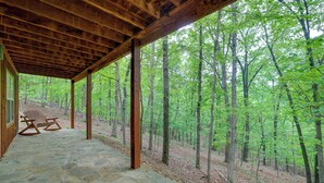 A covered stone patio with wooden beams, two rocking chairs, and a view of a forest.