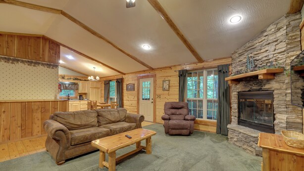 A cozy log cabin interior with a fireplace, wooden furniture, and a stone accent wall.