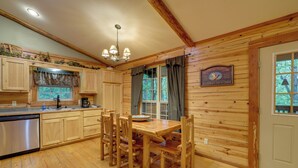 A wooden interior with a dining table and chairs, wooden cabinets, a built-in oven, and a window with curtains.