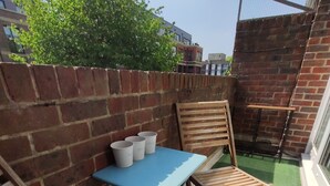 A small outdoor patio area with a blue table and two wooden chairs, a brick wall, and a green artificial turf floor. - Stylish Stay in Camberwell (London)