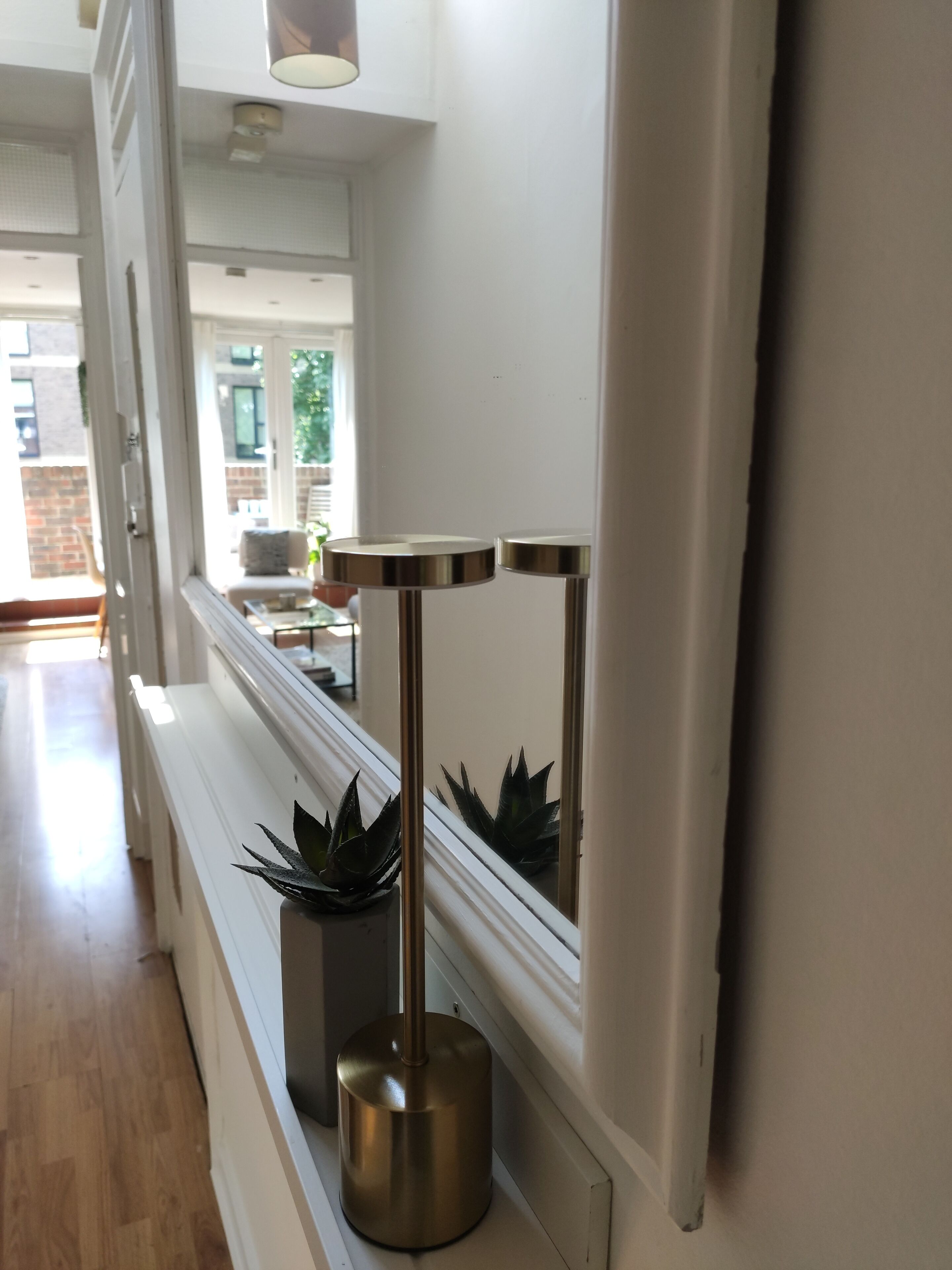 Un couloir avec un mur blanc, un plancher en bois et une fenêtre avec des stores.