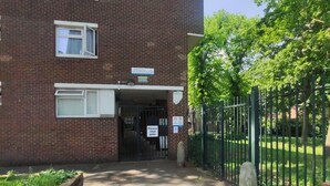 A brick building with a gated entrance, a sign indicating the address, and a pathway leading to the entrance. - Stylish Stay in Camberwell (London)