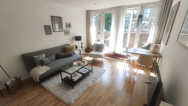 A modern living room with a grey sofa, coffee table, and a dining area with a table and chairs. - Stylish Stay in Camberwell (London)