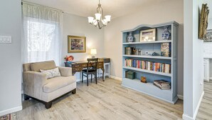 Una sala de estar con un sofá color crema, una mesa de comedor de madera con sillas, una estantería azul y un candelabro.