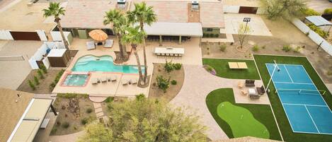 A residential property with a swimming pool, patio seating, a tennis court, and a small garden area.