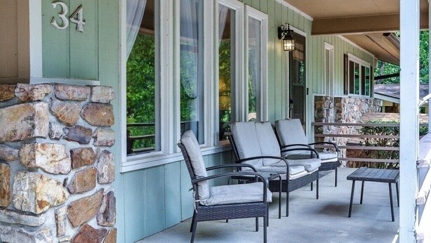 A covered porch with stone walls, numbered 34, featuring wicker chairs and a small table. - 05234 - 34 South Pego Way (Hot Springs)