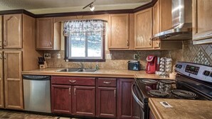 A kitchen with wooden cabinets, a stainless steel dishwasher, a stove, and a coffee maker. - 05234 - 34 South Pego Way (Hot Springs)