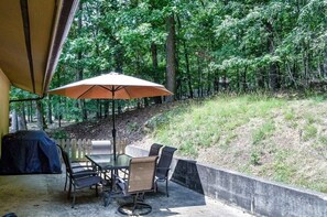 An outdoor patio with a table and chairs, a covered umbrella, and a view of a wooded area. - 05234 - 34 South Pego Way (Hot Springs)